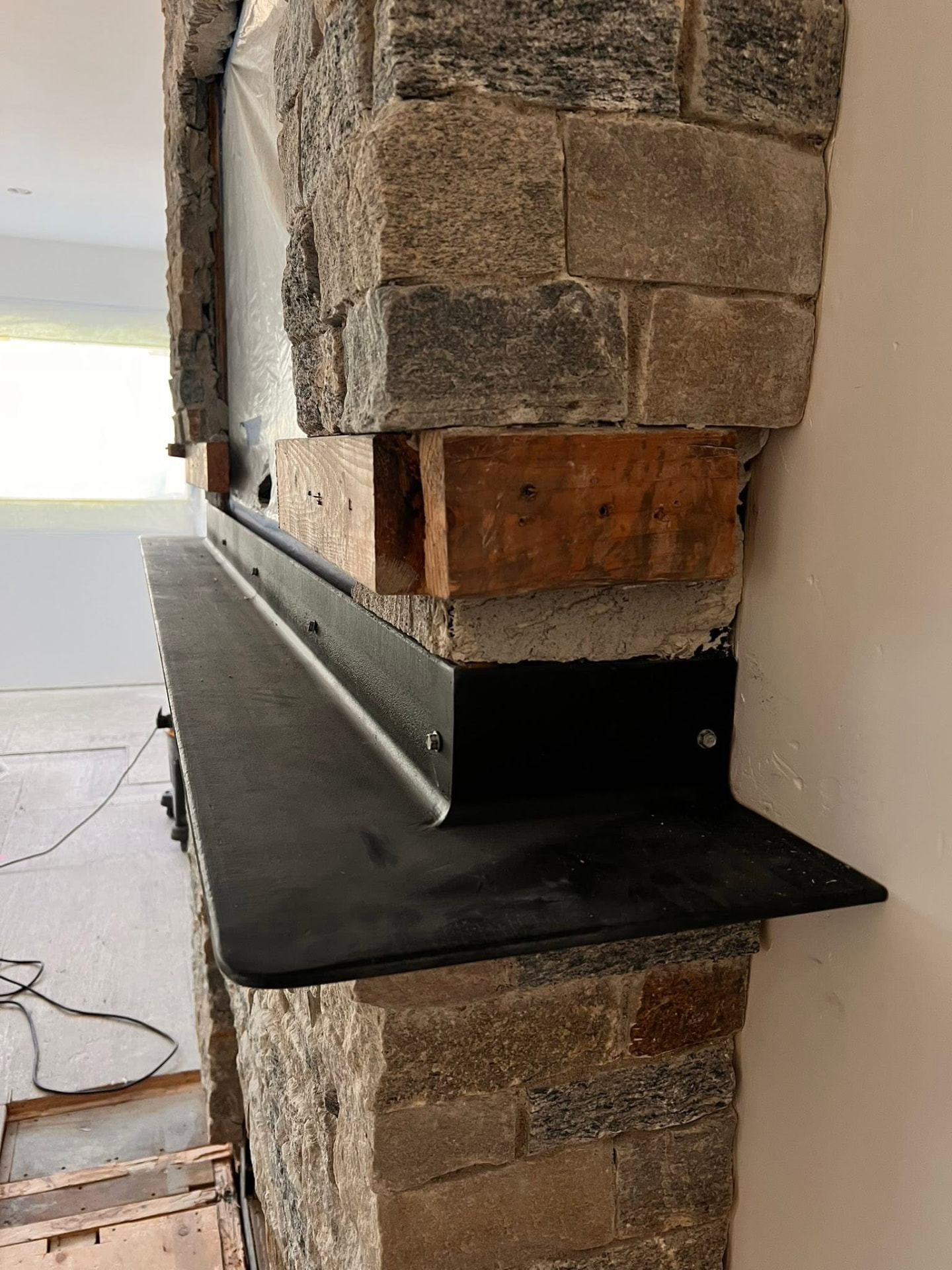 Close-up of a welded black steel fireplace mantle shelf mounted to a stone chimney