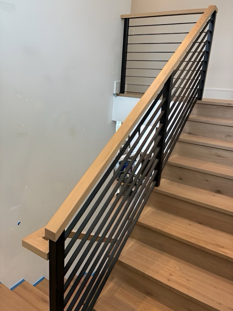 Modern staircase with light wood treads, wood handrail, and black metal horizontal balusters
