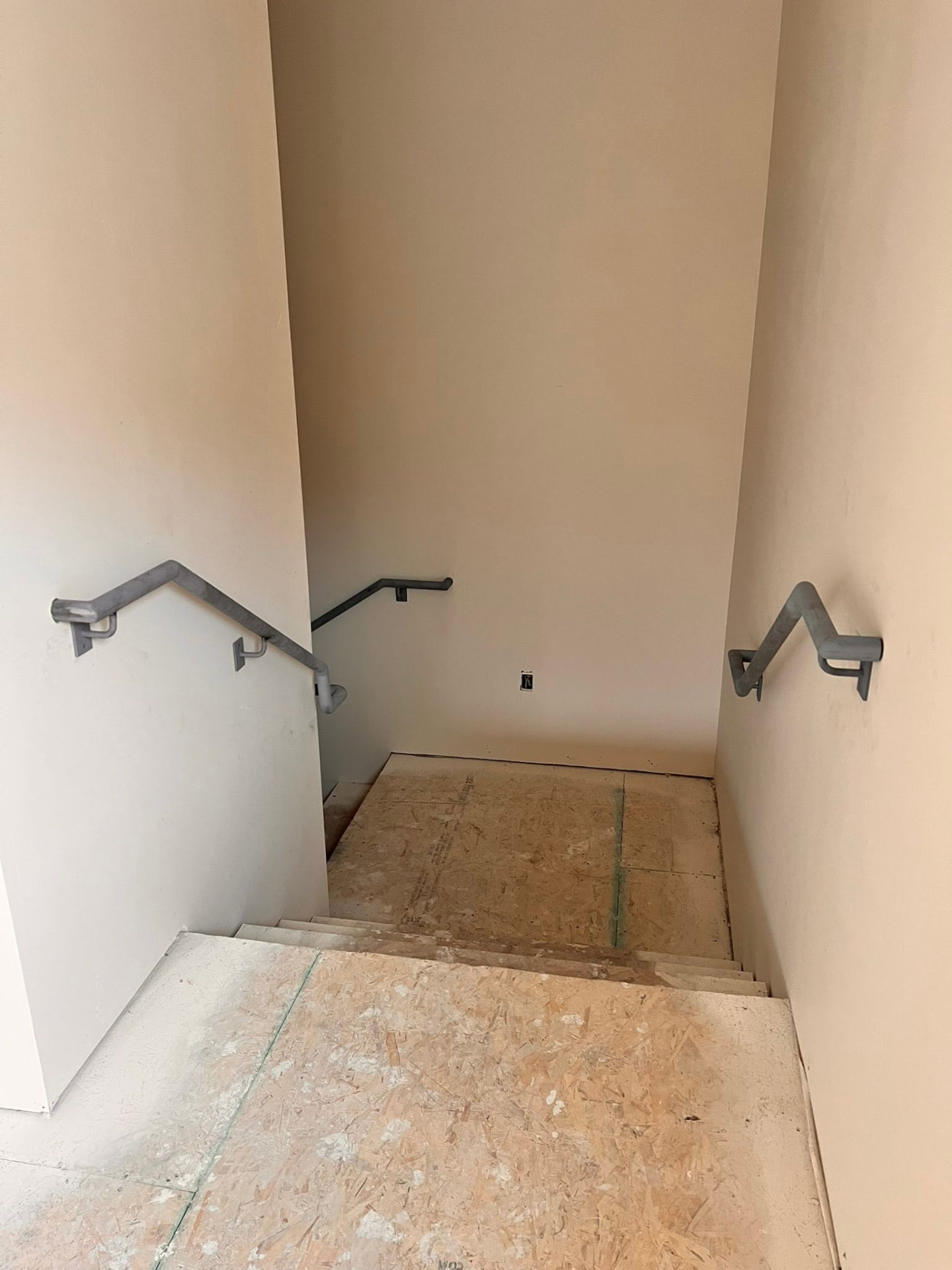 Grey metal wall-mounted handrails installed in a staircase under construction