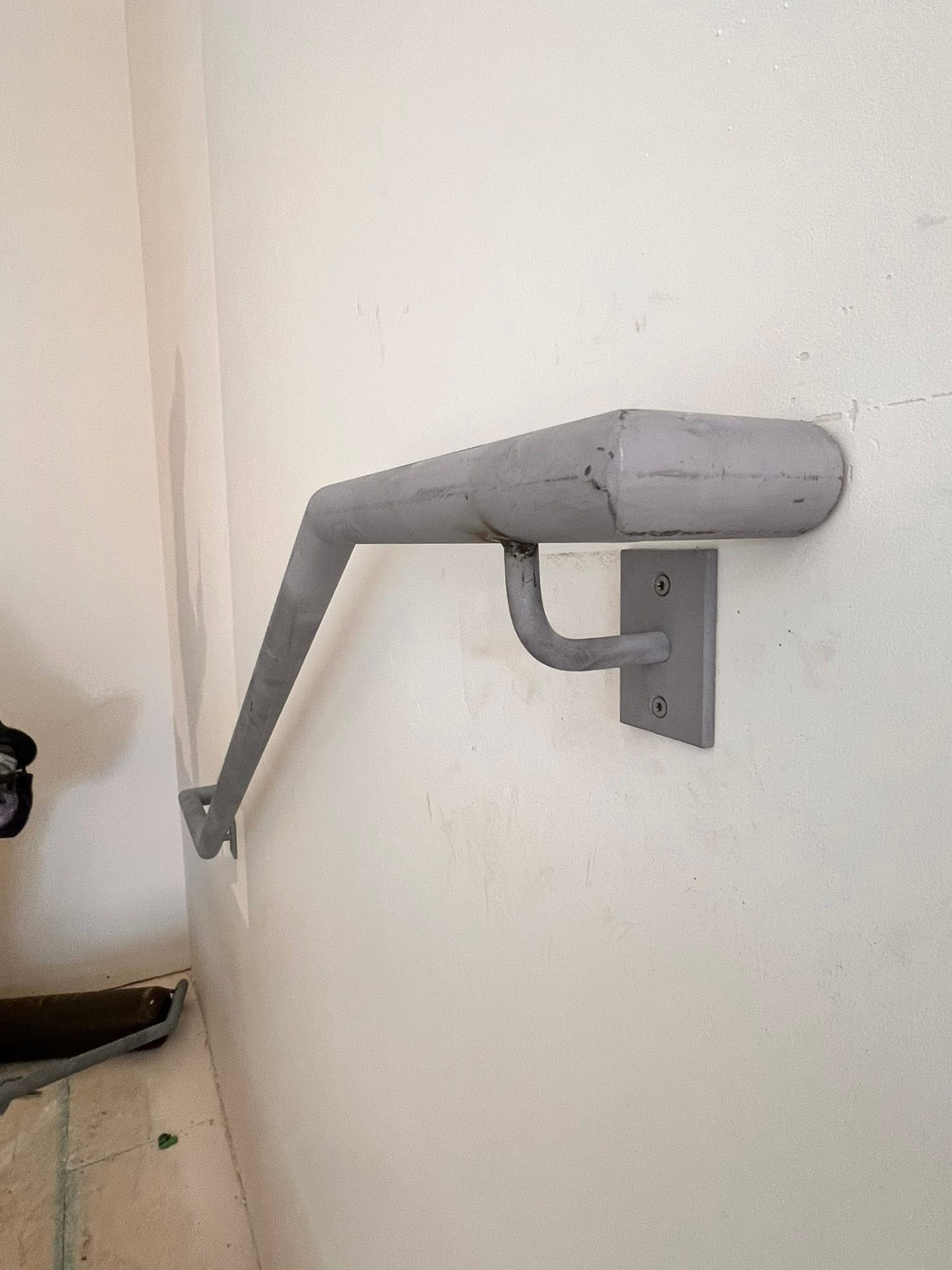 Grey metal wall-mounted handrail with industrial mounting plate on a white wall