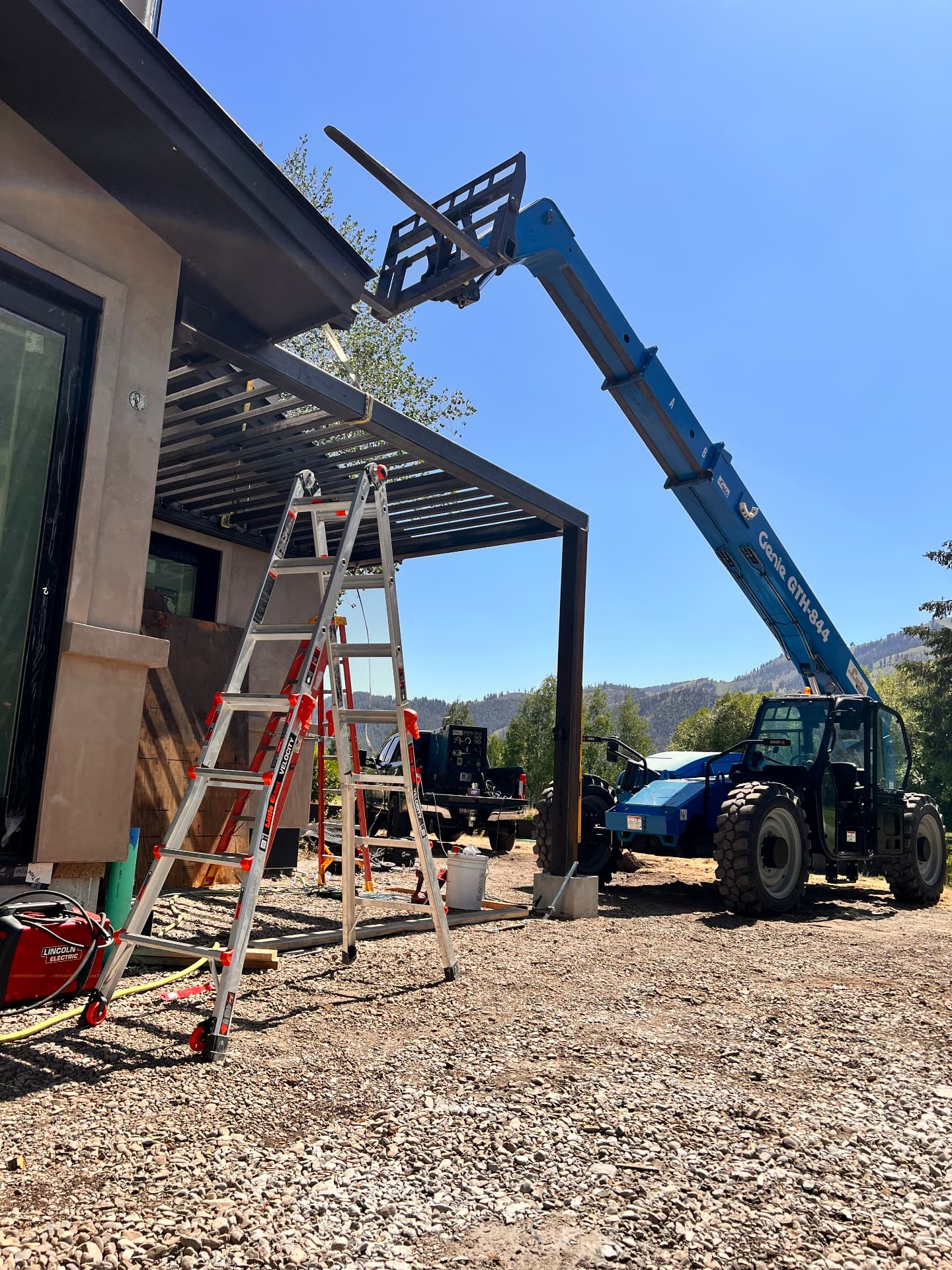 Crew using a telehandler to install a custom steel patio canopy at a residential jobsite