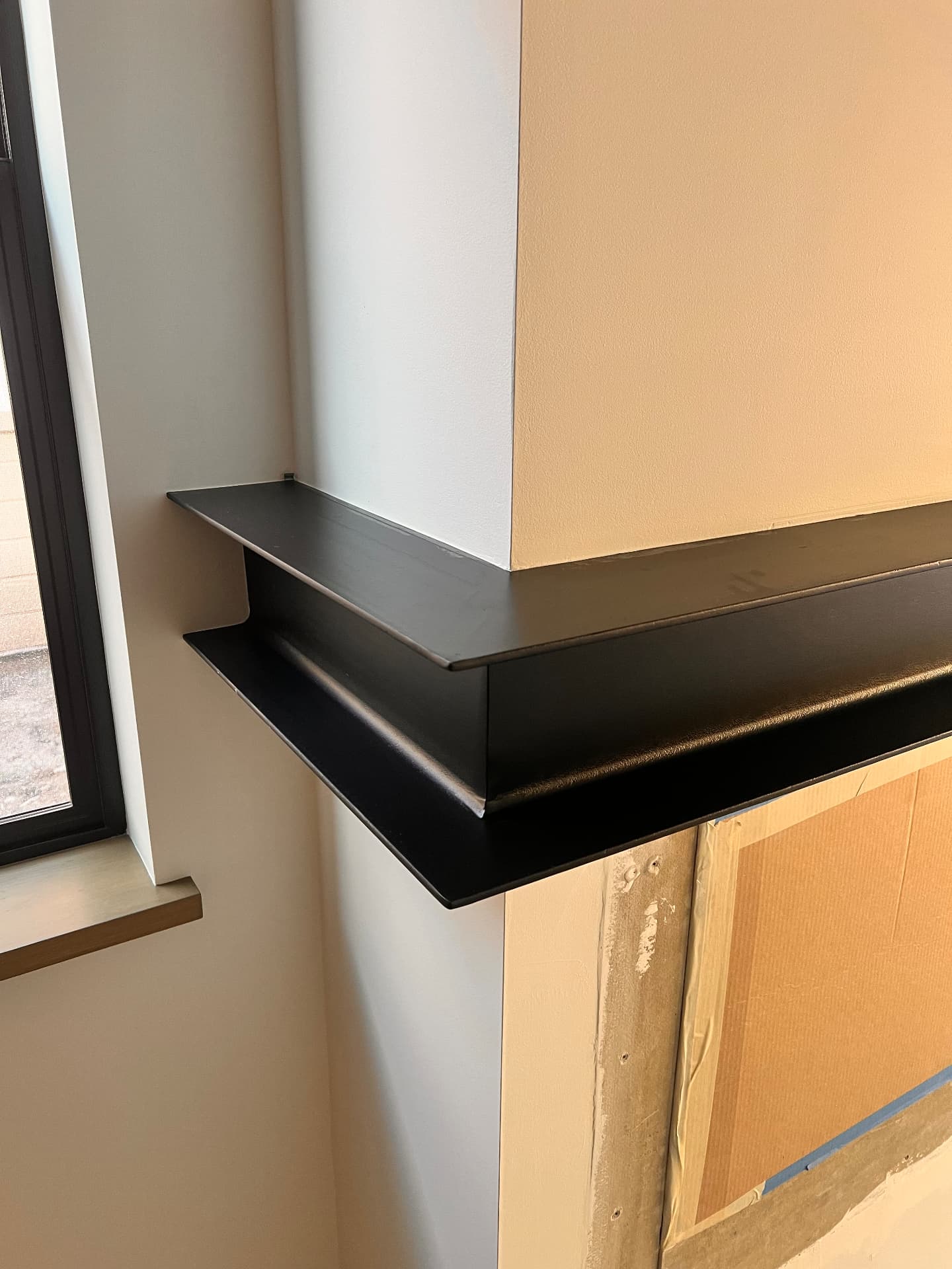 Side view of a custom black steel wraparound fireplace mantle beside a window