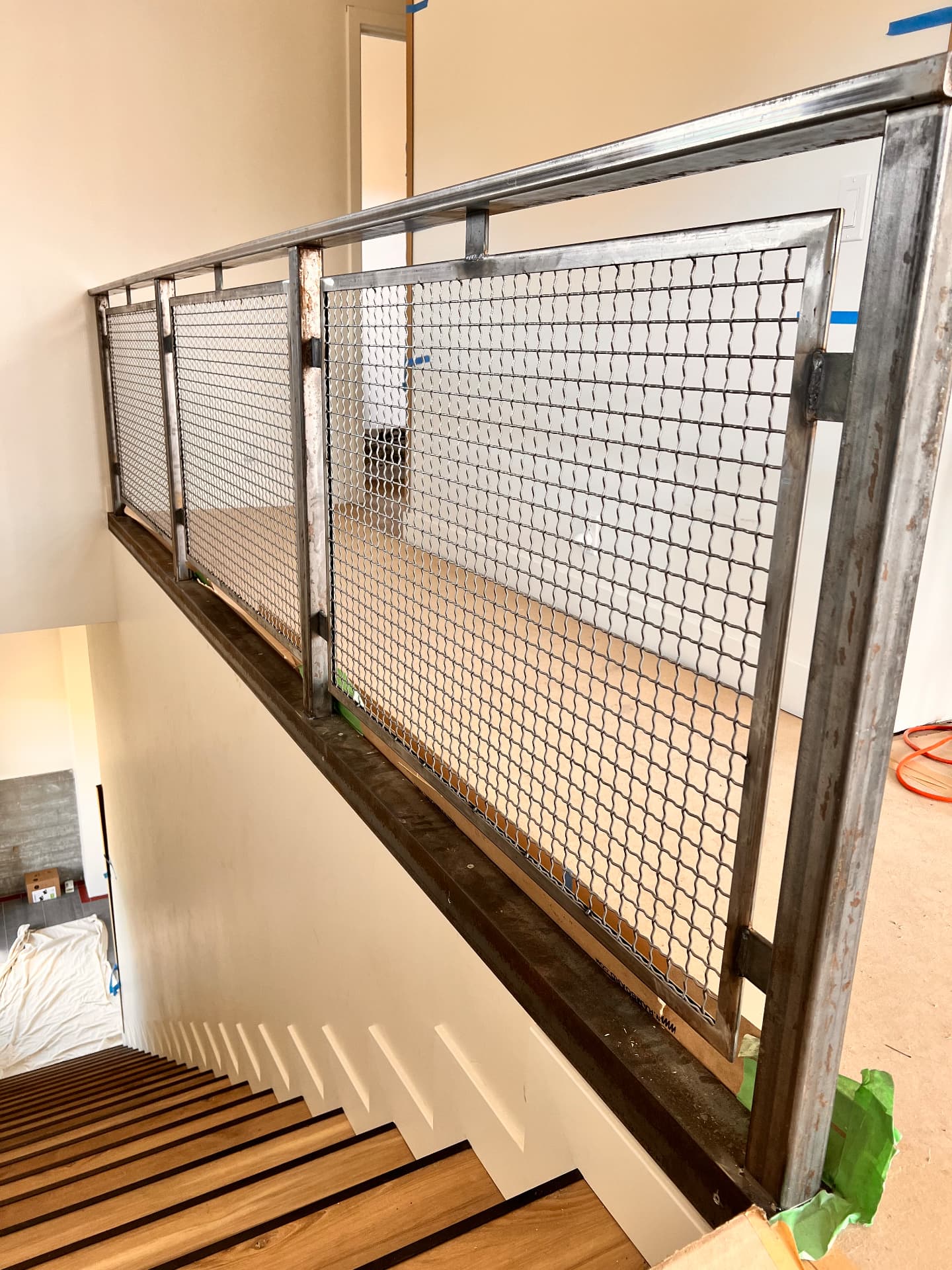Custom steel mesh guardrail installed beside an interior wood staircase