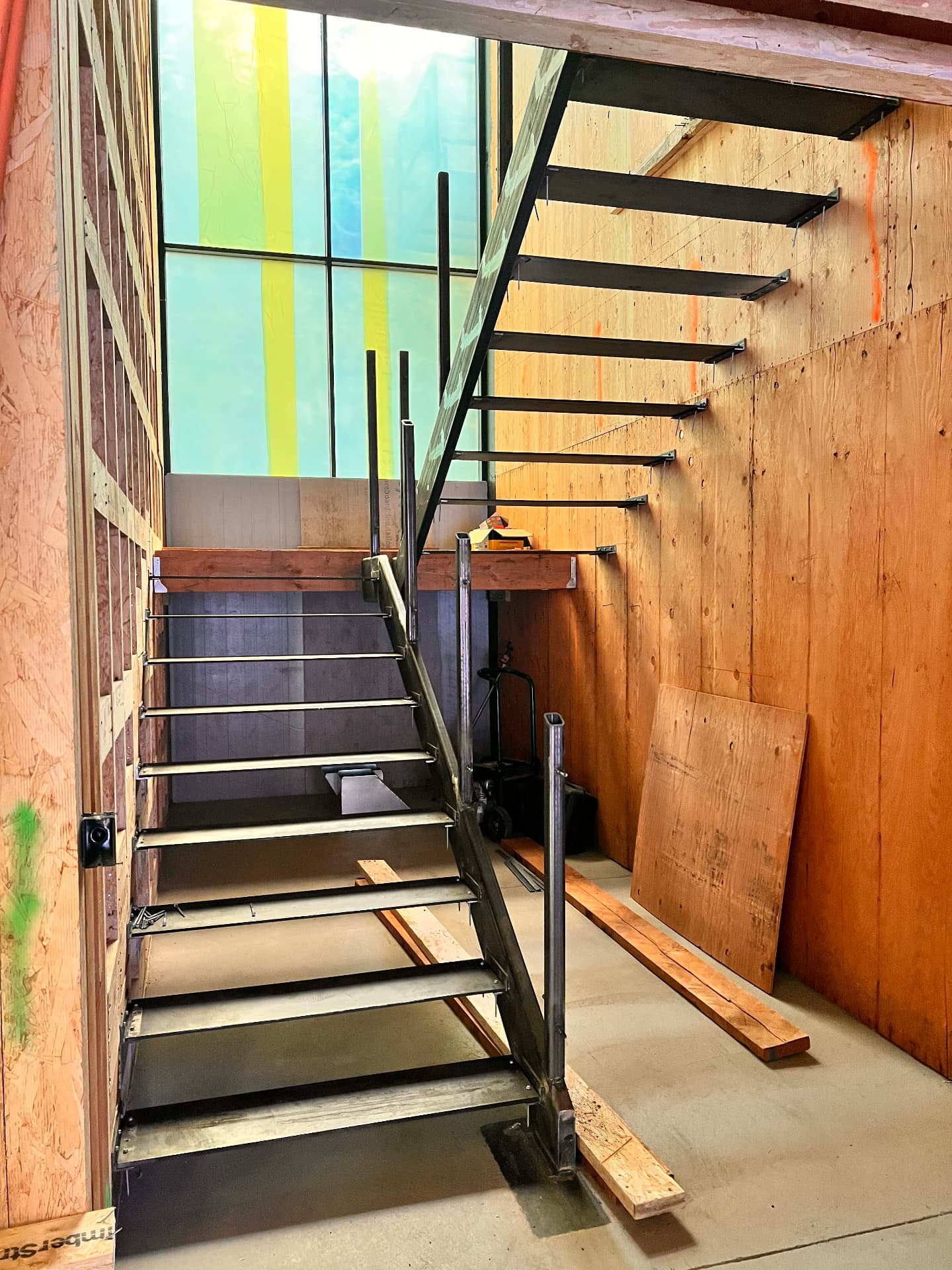 Floating steel staircase with open risers and metal railing posts beside a tall window