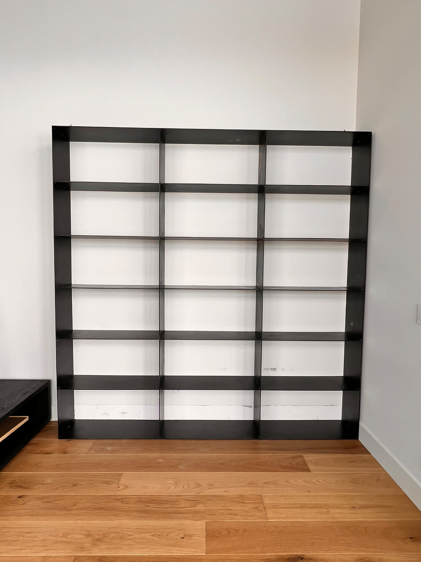 Wide custom black steel display shelving with slim horizontal shelves in a finished room
