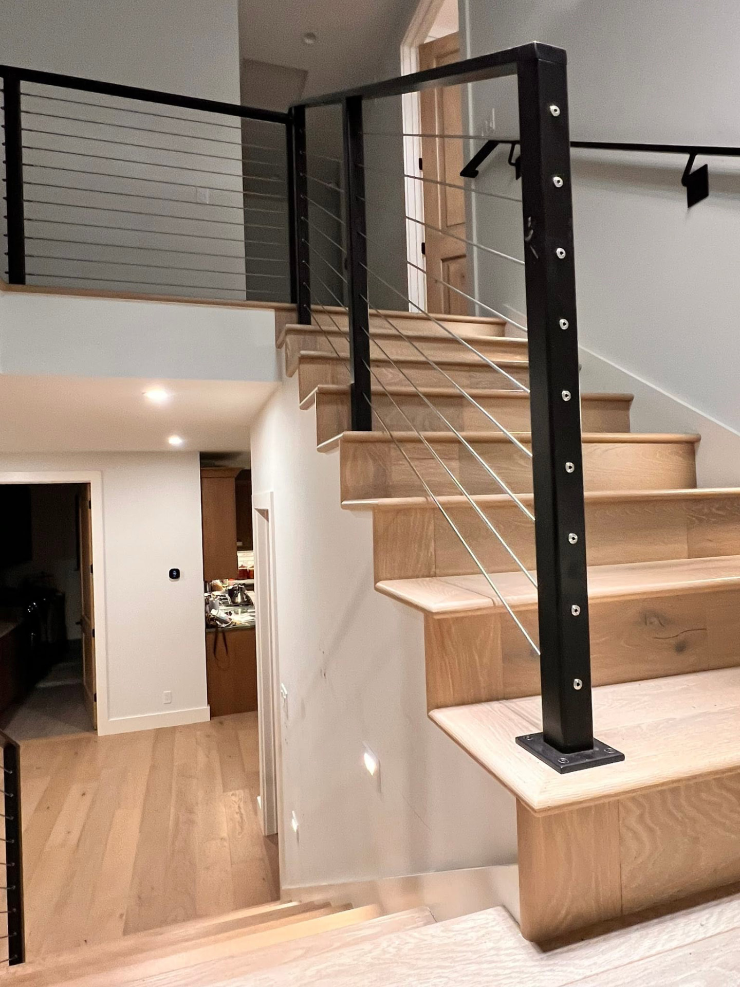 Indoor wooden staircase with black metal posts and horizontal cable infill railing