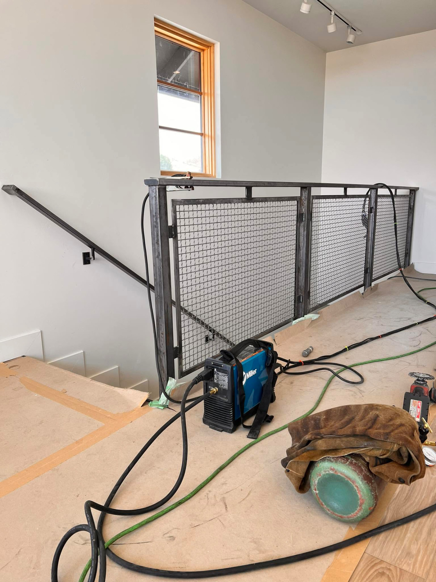 Metal railing with wire mesh infill installed on a landing, with a blue Miller welding machine