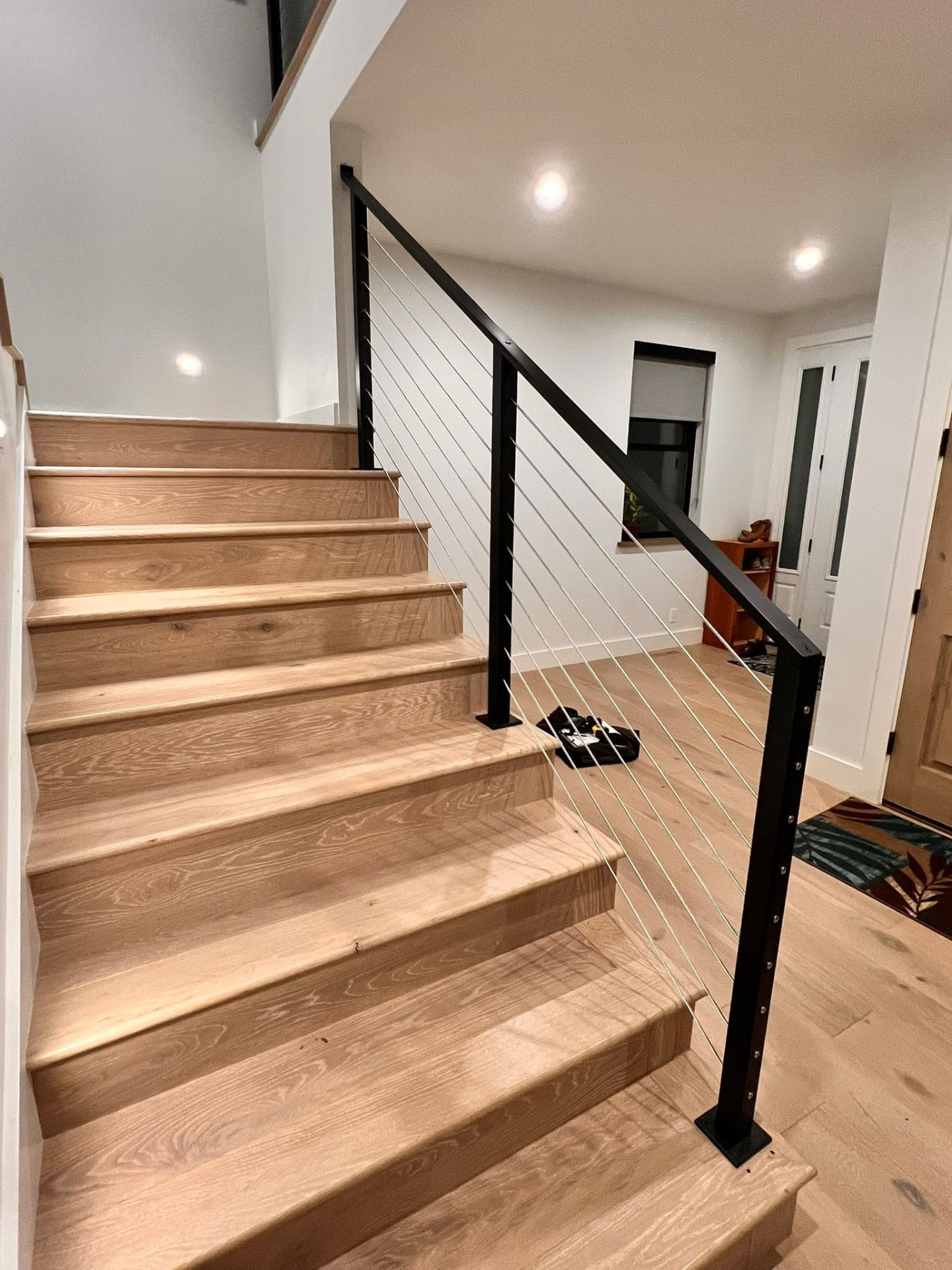 Bottom-up view of a wooden staircase with a black metal handrail and cable infill