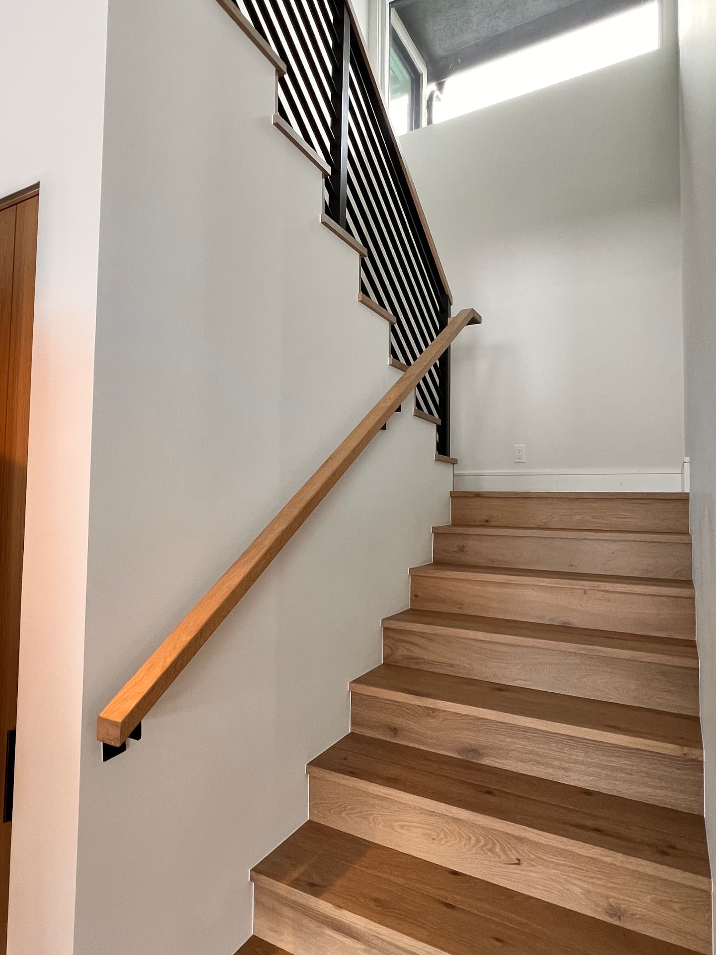 Finished wood staircase with black steel railing and matching wall-mounted wooden handrail