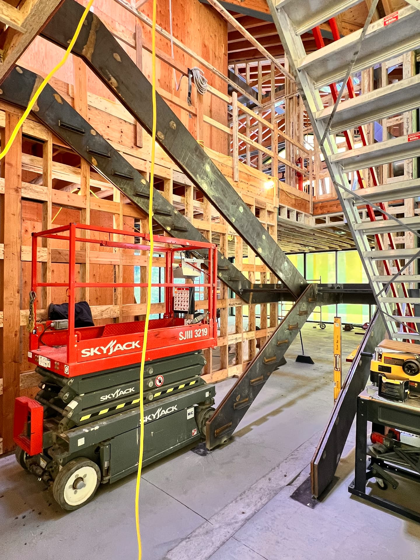 Steel stair stringers installed in a wood-framed home under construction, with a scissor lift beside them