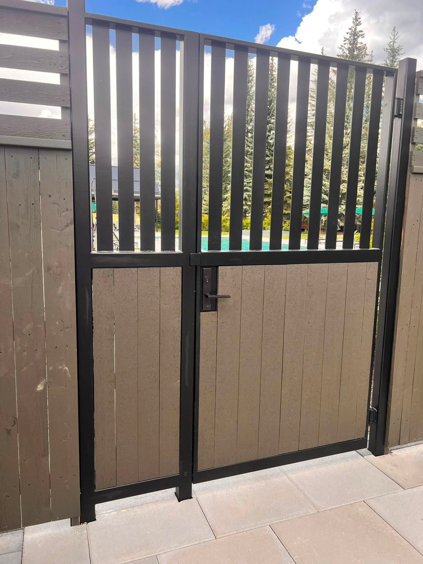 Finished black metal gate with vertical slats and wooden panels set into a fence