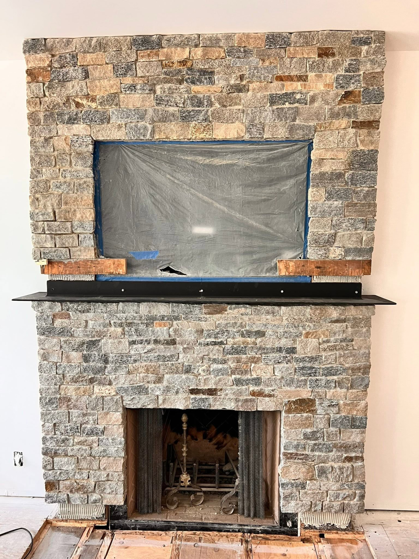 Stone fireplace fitted with a custom black steel TV mount and floating steel shelf