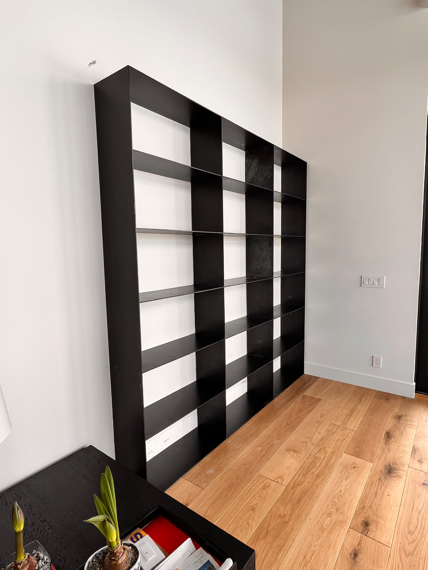 Floor-to-ceiling custom black steel shelving installed against a white interior wall