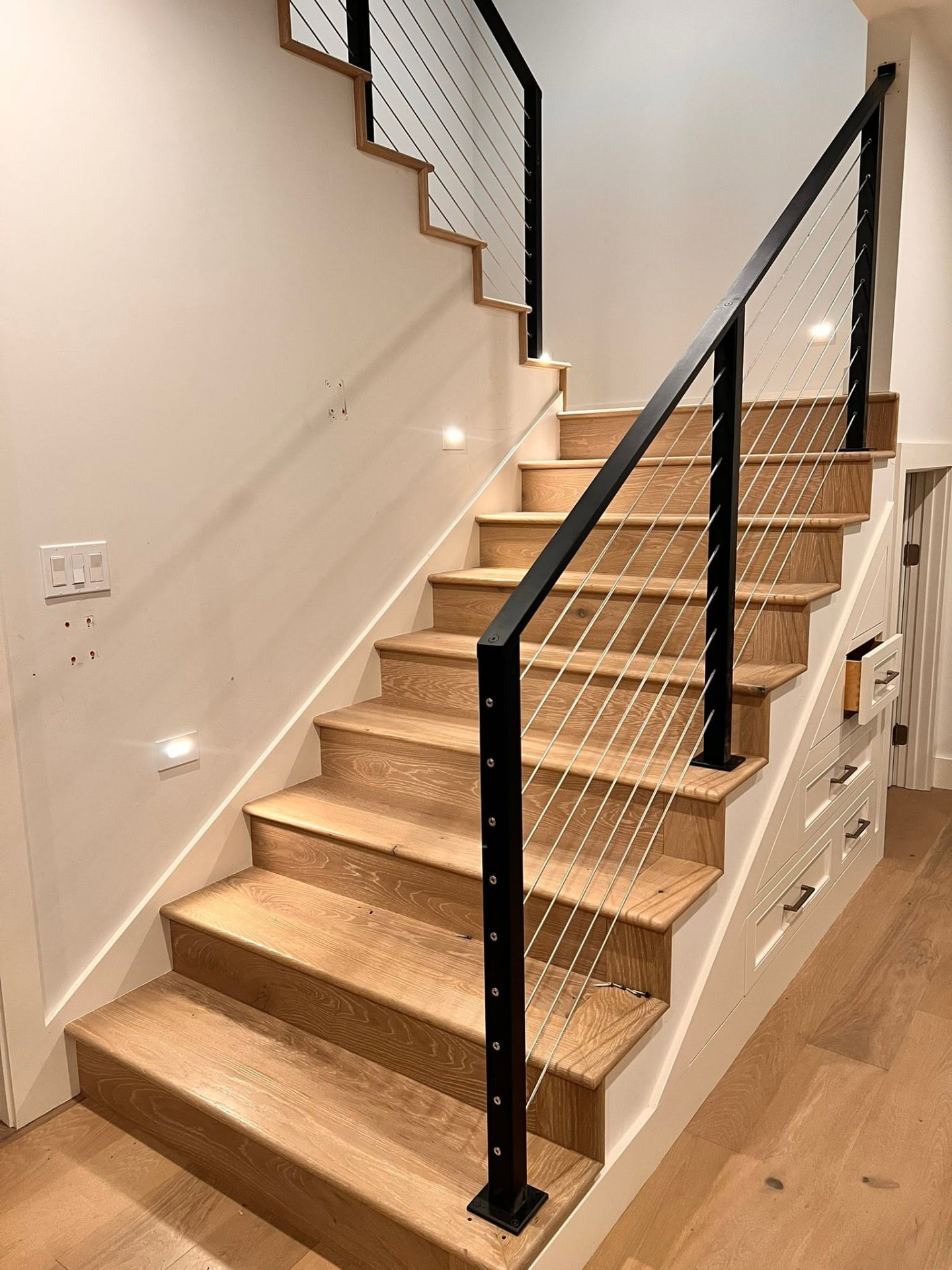 Wooden indoor staircase featuring a black metal handrail with horizontal cable infill